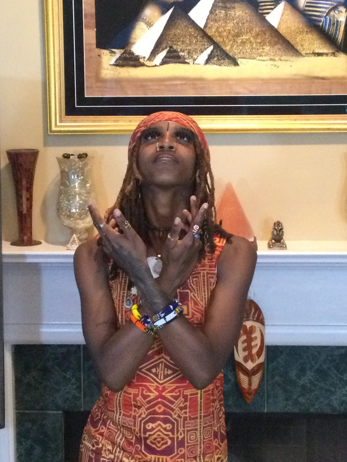 Black Queen in front of Pyramid in a living room wearing a burgundy and gold afrofuturistic print